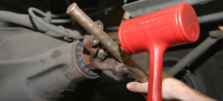 A person installing a yoke on a vehicle using a red mallet.