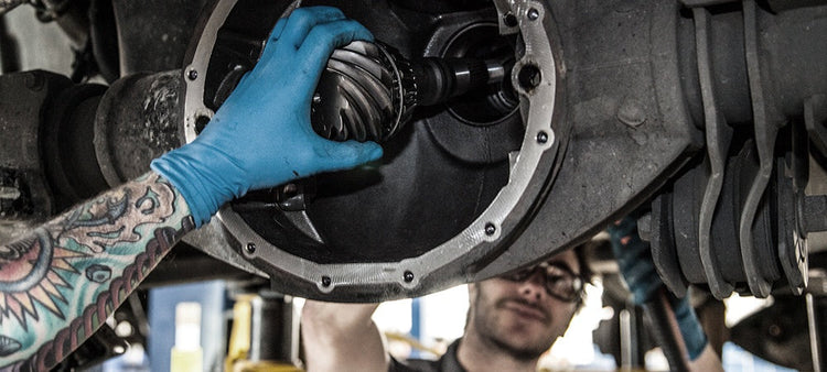 People working on the rear diffential of a vehicle.